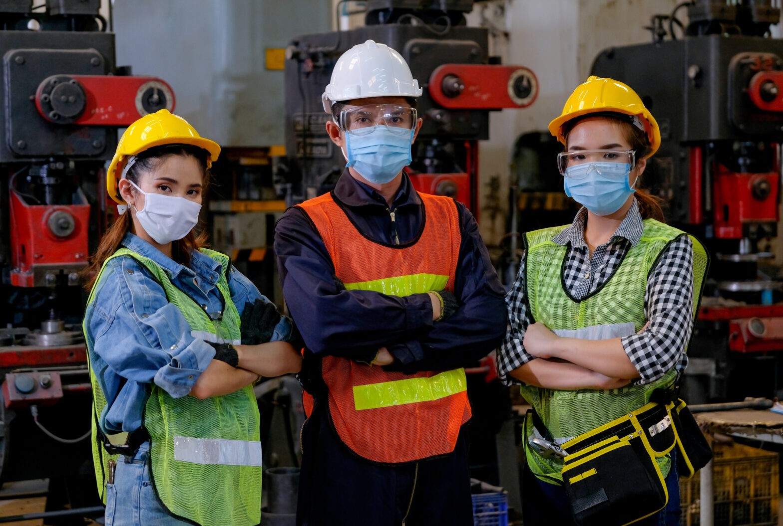 Group of man and woman workers with mask stand with confident action in the factory workplace and various machine as background