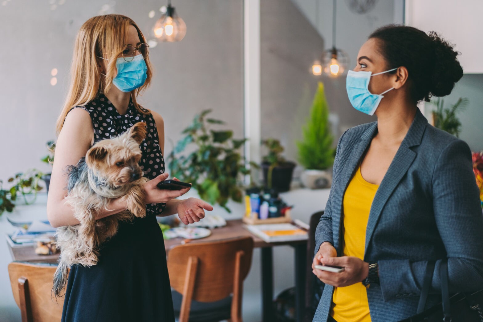Businesswomen with face masks talking in office, COVID-19 pandemic